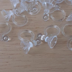 May include: A close-up of a group of clear plastic earring backs. The backs are designed to be used with clip-on earrings.