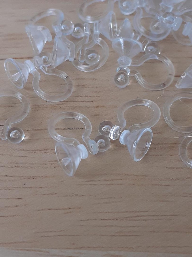 May include: A close-up of a group of clear plastic earring backs. The backs are designed to be used with clip-on earrings.