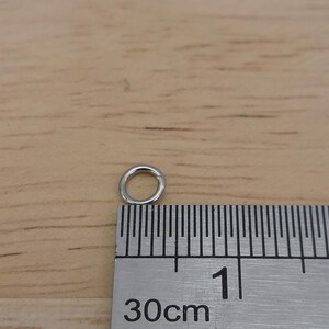 May include: A silver jump ring measuring approximately 1 cm in diameter, shown next to a ruler marked in centimeters.
