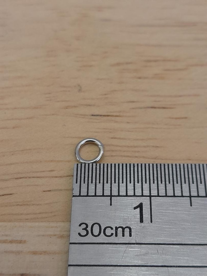 May include: A silver jump ring measuring approximately 1 cm in diameter, shown next to a ruler marked in centimeters.