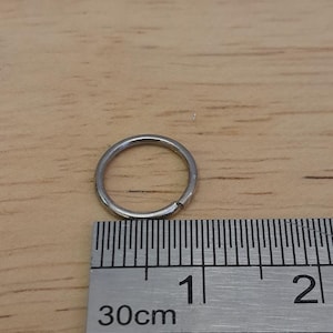 May include: A silver metal ring measuring 1 cm in diameter, next to a ruler marked in centimeters.
