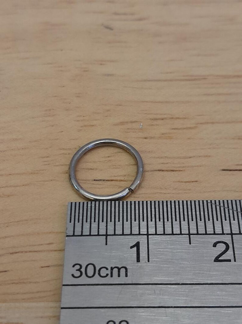 May include: A silver metal ring measuring 1 cm in diameter, next to a ruler marked in centimeters.