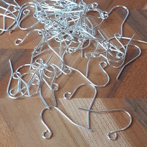 May include: A pile of silver earring hooks on a wooden surface. The hooks are made of metal and have a simple design.