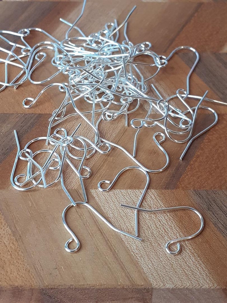 May include: A pile of silver earring hooks on a wooden surface. The hooks are made of metal and have a simple design.