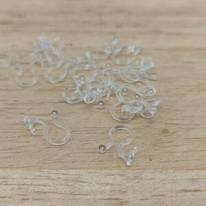 May include: A pile of clear plastic curtain hooks on a wooden surface.