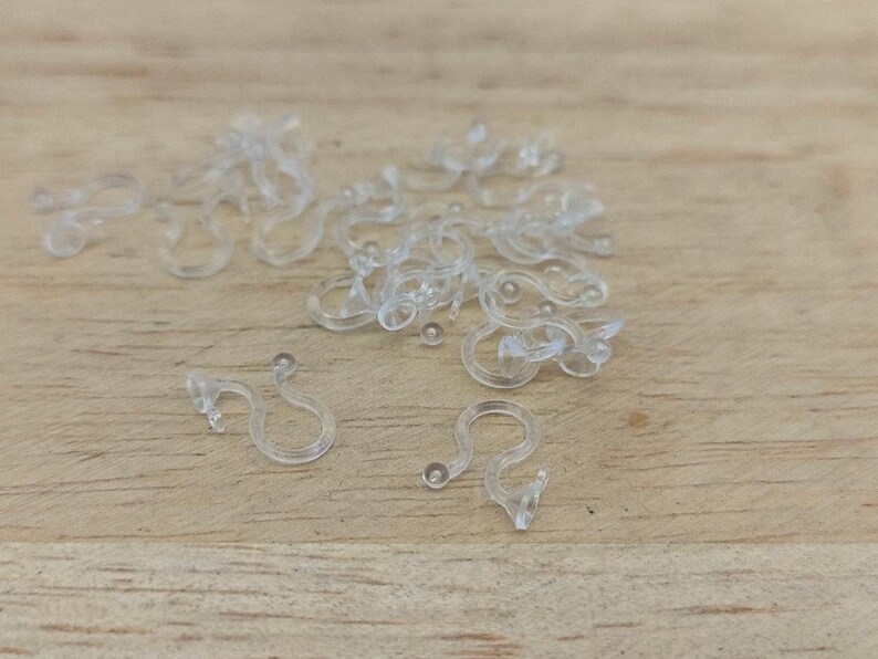 May include: A pile of clear plastic curtain hooks on a wooden surface.