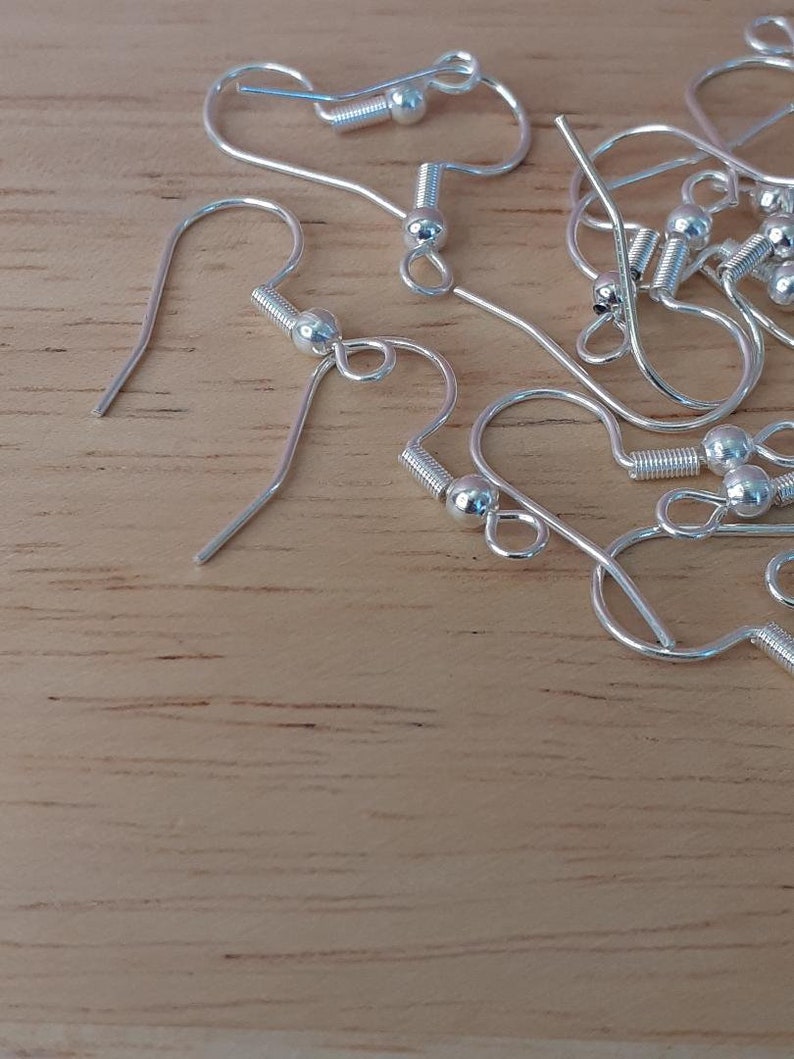 Puede incluir: Primer plano de un mont&oacute;n de ganchos para pendientes de plata con una peque&ntilde;a bola al final de cada gancho.