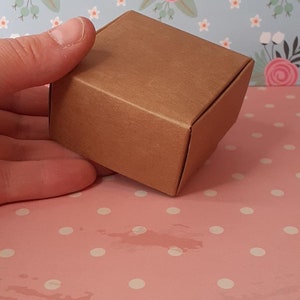 K&ouml;nnte beinhalten: Eine kleine braune Schachtel aus Pappe mit einer strukturierten Oberfl&auml;che. Die Schachtel ist leer und bereit, mit einem Geschenk oder anderen kleinen Gegenst&auml;nden gef&uuml;llt zu werden.