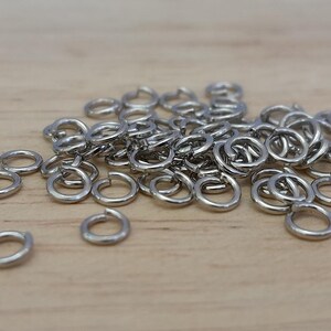 May include: A pile of silver jump rings, a type of jewelry finding, on a wooden surface.