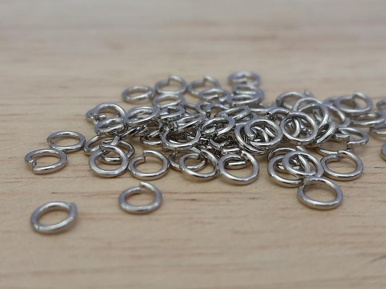 May include: A pile of silver jump rings, a type of jewelry finding, on a wooden surface.