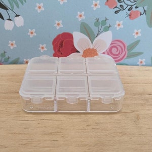 May include: A clear plastic storage box with six compartments. The box is empty and has a smooth surface.