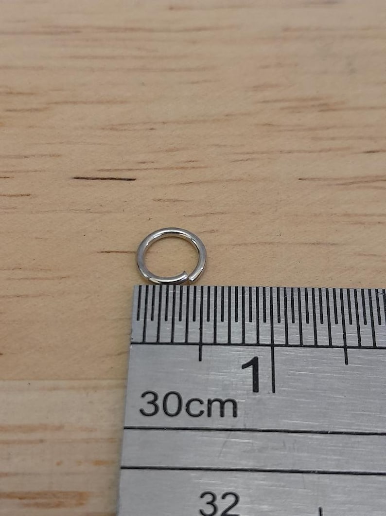 May include: A silver jump ring measuring 1 cm in diameter, next to a ruler.