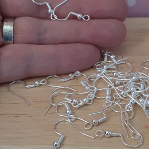 Puede incluir: Primer plano de un mont&oacute;n de ganchos para pendientes de plata con una peque&ntilde;a bola al final de cada gancho.