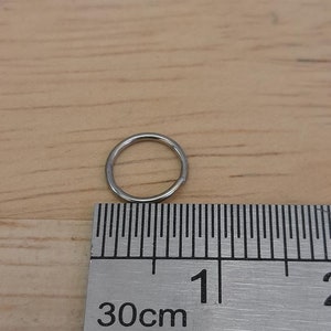 May include: A silver jump ring measuring approximately 1 cm in diameter, next to a ruler marked in centimeters.