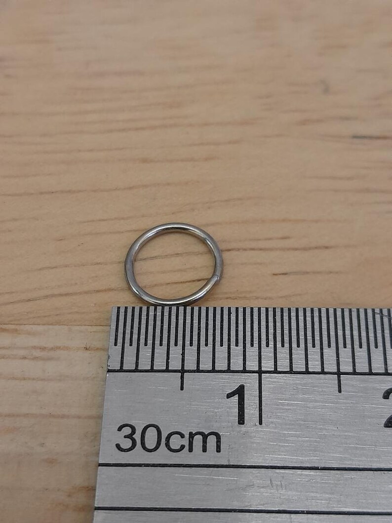 May include: A silver jump ring measuring approximately 1 cm in diameter, next to a ruler marked in centimeters.