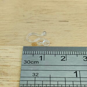 May include: Close-up of a clear plastic curtain clip with a ruler in the background. The ruler shows measurements in centimetres.