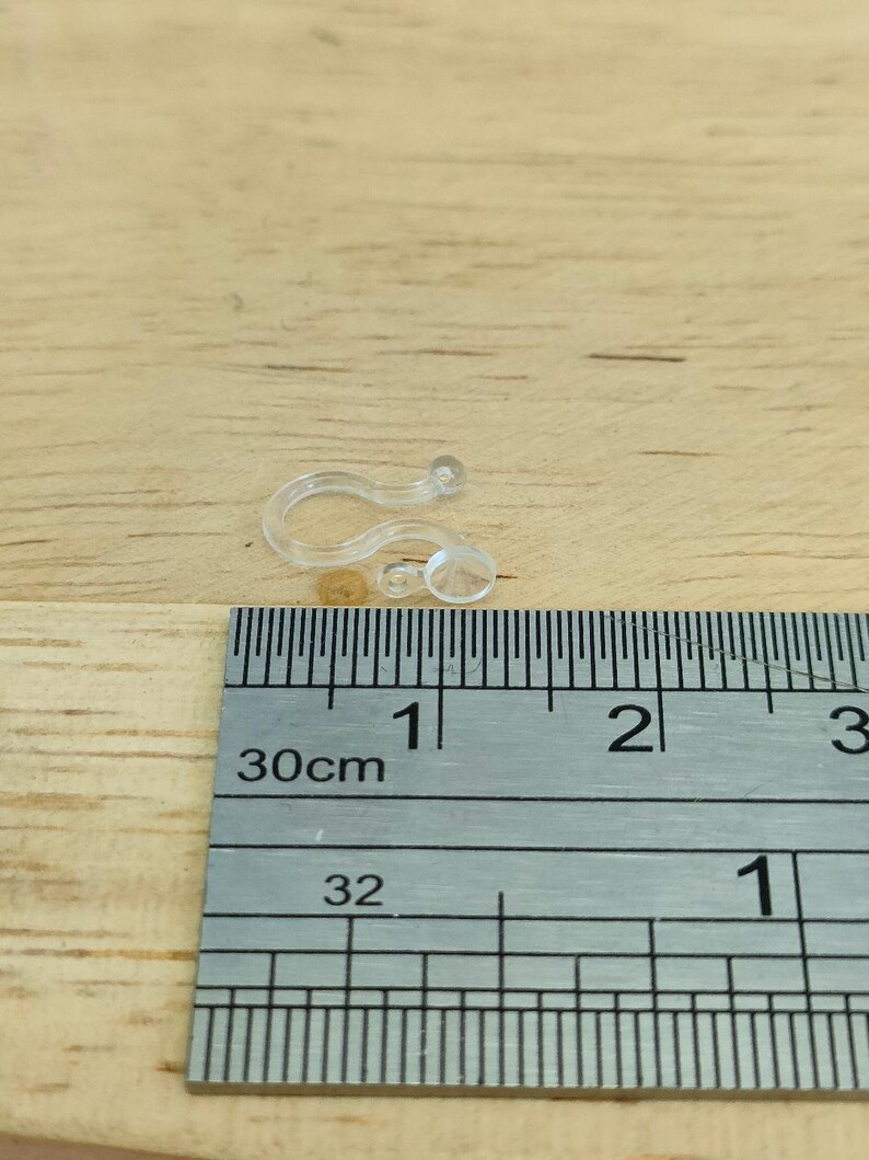May include: Close-up of a clear plastic curtain clip with a ruler in the background. The ruler shows measurements in centimetres.