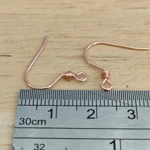 May include: Two rose gold earring hooks with a twisted wire design. The hooks are measured against a ruler, showing they are approximately 1 inch long.