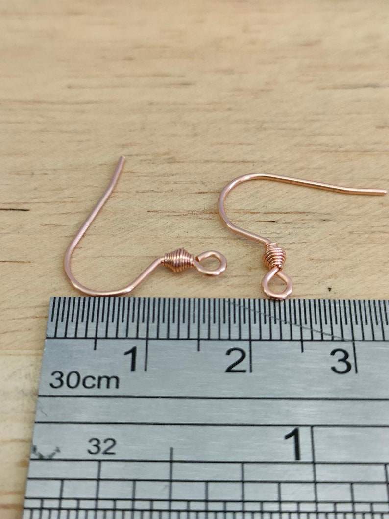 May include: Two rose gold earring hooks with a twisted wire design. The hooks are measured against a ruler, showing they are approximately 1 inch long.