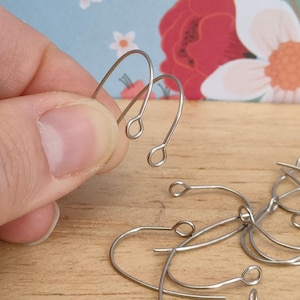 May include: A close-up of silver earring hooks. The hooks are made of metal and have a simple design. They are perfect for making earrings.