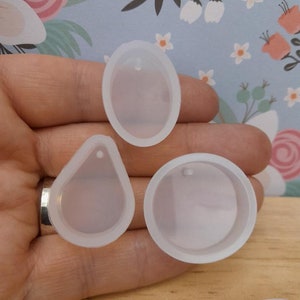 May include: Three clear silicone moulds for resin casting. The moulds are shaped like a teardrop, a circle, and an oval. Each mould has a small hole at the top for adding a bail or jump ring.