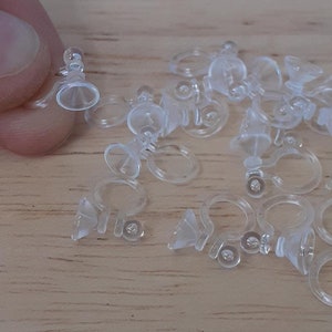 May include: A group of clear plastic earring backs with a small cone-shaped piece on the bottom. The backs are designed to be used with stud earrings.