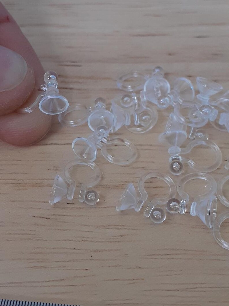 May include: A group of clear plastic earring backs with a small cone-shaped piece on the bottom. The backs are designed to be used with stud earrings.