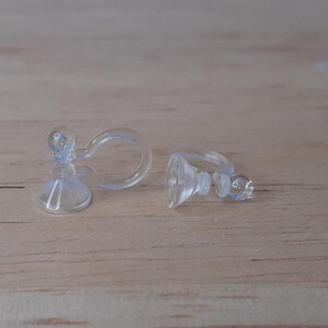 May include: Two clear plastic earring backs. The backs are designed to clip onto the back of an earring and have a suction cup to hold the earring in place.