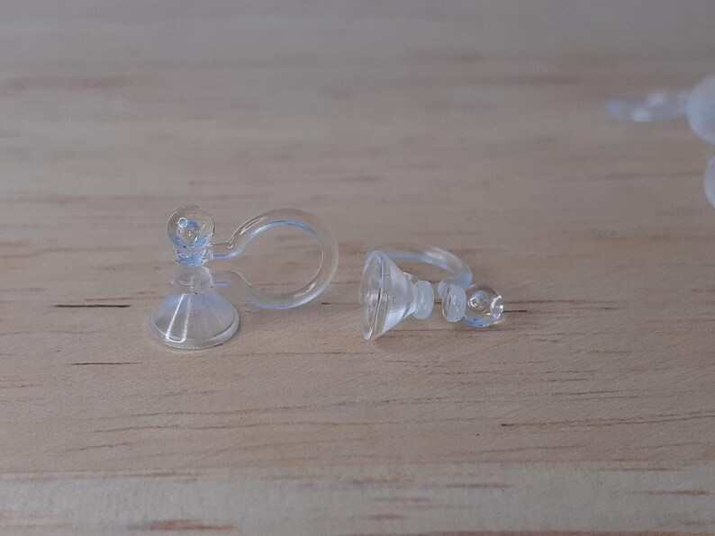 May include: Two clear plastic earring backs. The backs are designed to clip onto the back of an earring and have a suction cup to hold the earring in place.