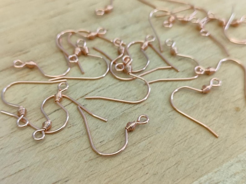 May include: A close-up of a group of rose gold earring hooks. The hooks are made of metal and have a small, twisted loop at the top.
