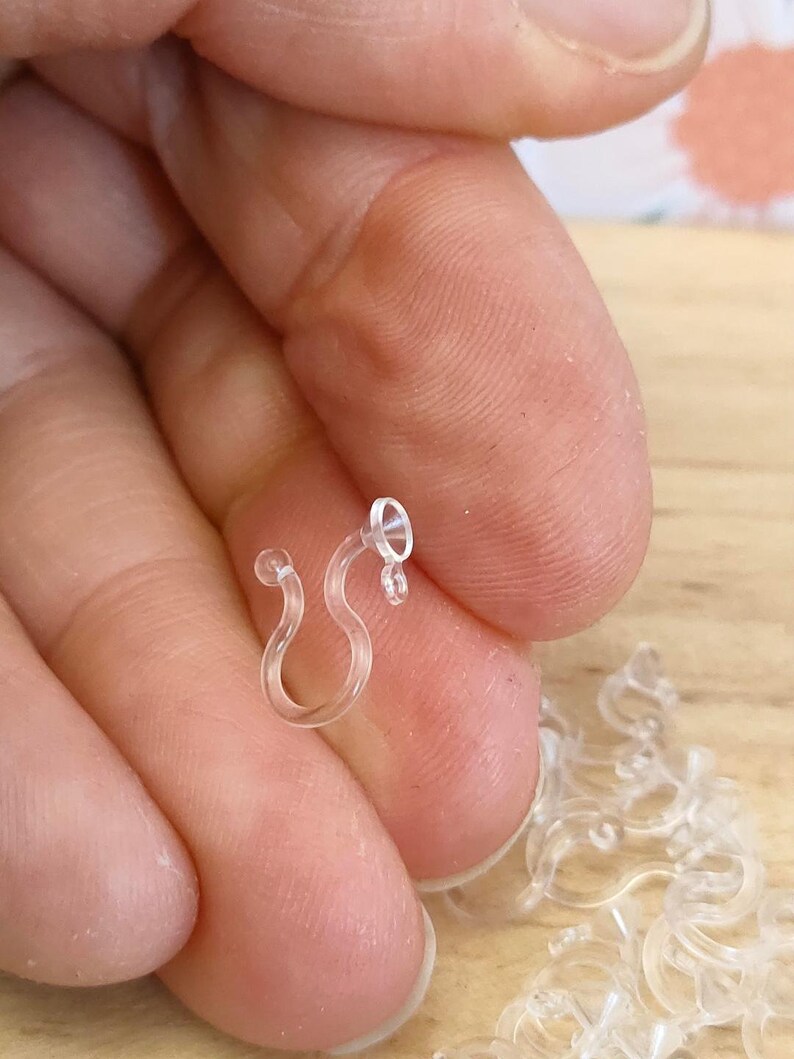 May include: Close-up of a clear plastic hook, a common type of hook used for hanging items like Christmas lights or other decorations.