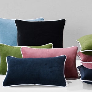 May include: A set of decorative throw pillows with white piping. The pillows are made of velvet and come in a variety of colors, including blue, black, green, pink, and navy.