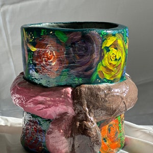 May include: Hand-painted ceramic planter with a dark green base and a textured, bulbous midsection. The planter is adorned with colorful roses in shades of red, yellow, and orange. The design includes a dark green rim with painted leaves.