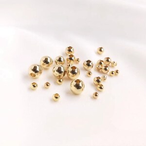 May include: A collection of gold-colored metal beads of various sizes. The beads are round and have a smooth, shiny finish.