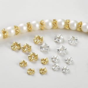 Peut inclure: Une collection d'entretoises de perles en métal doré et argenté avec un design plissé. Les entretoises sont disposées en deux rangées sur un fond blanc.