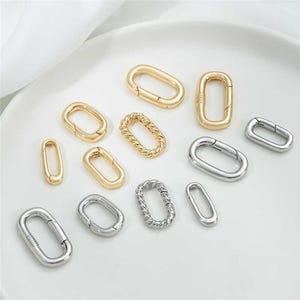 May include: Assortment of gold and silver oval-shaped metal clasps and connectors. Some clasps have a twisted rope design.