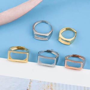 May include: Five silver rings with a rectangular opening. The rings are in different colours: silver, gold, rose gold.