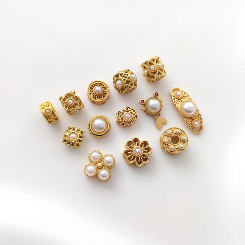 May include: Assortment of gold-toned metal beads with pearl accents. The beads feature various designs, including floral, geometric, and ornate patterns.