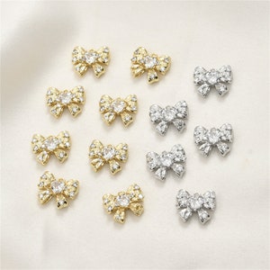 Könnte beinhalten: Eine Sammlung von goldenen und silbernen Schleifenanhängern mit klaren Kristall-Akzenten. Die Anhänger sind perfekt, um Schmuck, Bastelarbeiten und anderen Projekten einen Hauch von Glanz zu verleihen.