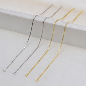 May include: Four delicate chains, two silver and two gold, with jump rings at the ends. The chains are arranged in a row on a white surface.