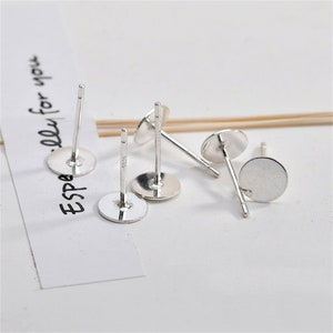 Può includere: Cinque perni per orecchini in argento con dorsi piatti rotondi. I perni sono lunghi circa 1 cm e i dorsi circa 1 cm di diametro.