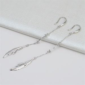 May include: A pair of silver dangle earrings with feather charms and a chain design.