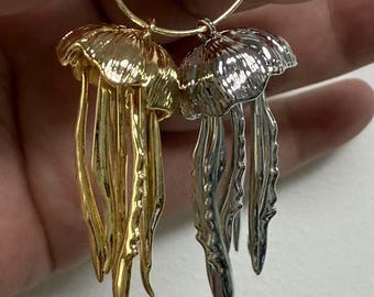May include: A pair of jellyfish earrings. One earring is gold-toned, the other is silver-toned. Each earring features a domed cap and flowing tentacles, suspended from a gold-colored hoop.