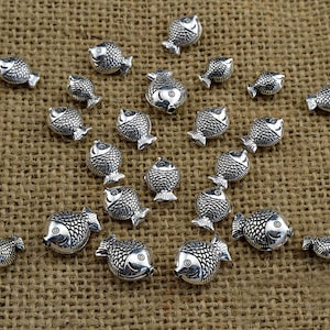 May include: A collection of silver-toned fish charms, arranged in a starburst pattern on a brown burlap background.