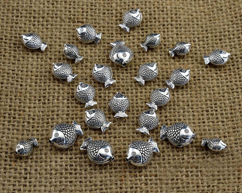 May include: A collection of silver-toned fish charms, arranged in a starburst pattern on a brown burlap background.
