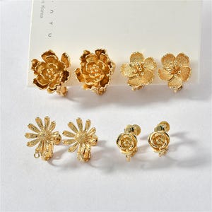 Peut inclure: Six paires de boucles d'oreilles clips en forme de fleur dorées. Les boucles d'oreilles présentent différents motifs floraux, notamment des roses, des marguerites et d'autres motifs floraux.