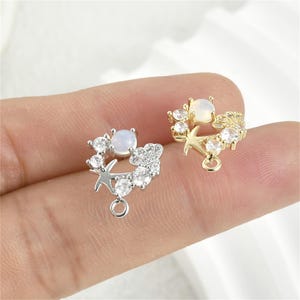 May include: Two gold-tone and silver-tone charm pendants featuring a white opal stone surrounded by clear rhinestones and a small bird design.