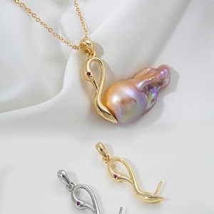 Pode incluir: Um pingente de cisne dourado com uma pérola rosa e um olho de pedra preciosa vermelha. O pingente é mostrado com uma corrente de ouro e um pingente de cisne prateado com um olho de pedra preciosa vermelha.
