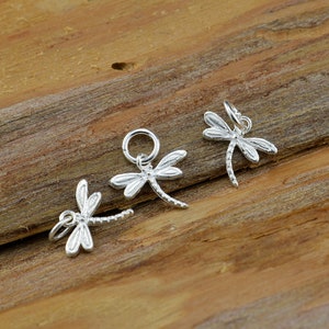 May include: Three silver dragonfly charms with a jump ring for attaching to jewelry. The dragonflies are detailed and have a delicate design.