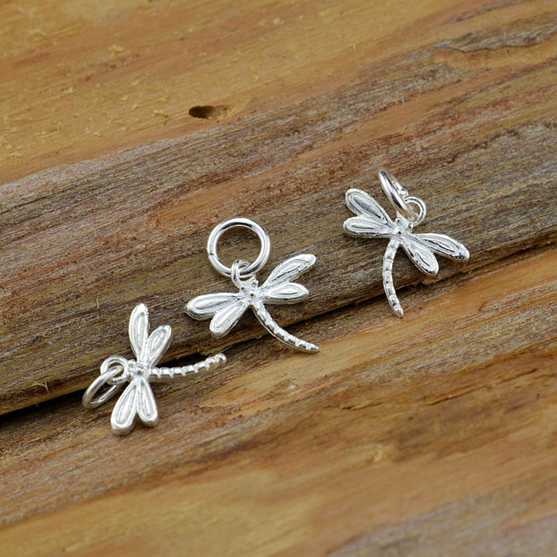 May include: Three silver dragonfly charms with a jump ring for attaching to jewelry. The dragonflies are detailed and have a delicate design.